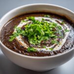 Close-up of a creamy, dark black bean soup topped with a swirl of cream and fresh cilantro.