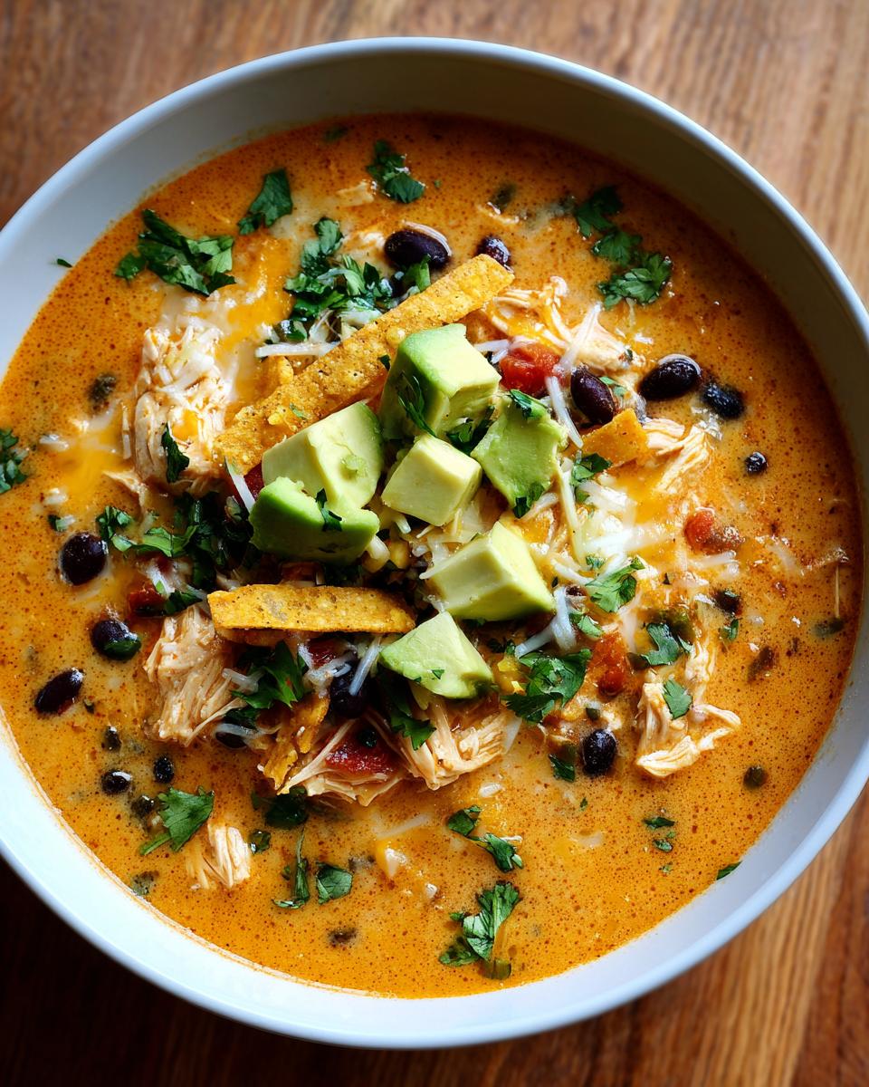 Overhead view of a creamy bowl of chicken tortilla soup topped with shredded chicken, black beans, avocado, and cilantro.