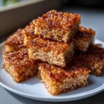 A stack of golden brown, caramelized crispy rice squares piled high on a white plate.
