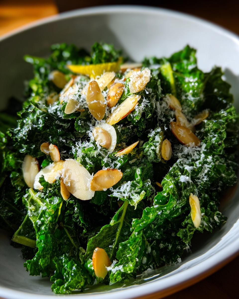 Close-up of a vibrant kale salad topped with sliced almonds, grated Parmesan, and a lemon wedge.