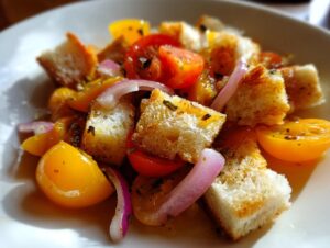 Close-up of a vibrant panzanella salad featuring toasted bread cubes, halved yellow and red cherry tomatoes, and slivers of red onion.