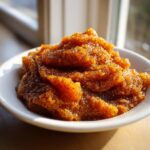 A close-up of thick, glistening homemade pear butter piled high in a white bowl, catching the sunlight.