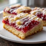 A close-up of a square cherry pie bars slice showing the thick cherry filling, crumb topping, and white icing drizzle.