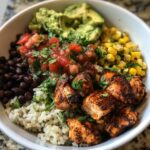 Close-up of a colorful chicken burrito bowl featuring seasoned chicken, rice, black beans, corn, salsa, and guacamole.