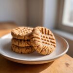 A stack of four classic peanut butter cookies with the traditional criss-cross fork marks, sitting on a light plate.