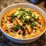 A close-up of a bowl of creamy chicken tortilla soup loaded with shredded chicken, black beans, and topped with avocado cubes.