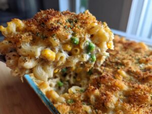 A spoonful of creamy tuna pasta bake with corn and peas, showing a golden-brown crispy breadcrumb topping.