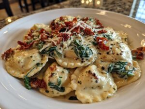 A close-up shot of creamy Tuscan ravioli tossed in a rich cream sauce with spinach and topped with sun-dried tomatoes and grated Parmesan.