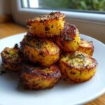 A stack of golden brown, crispy oven roasted potatoes seasoned with dark herbs like rosemary.