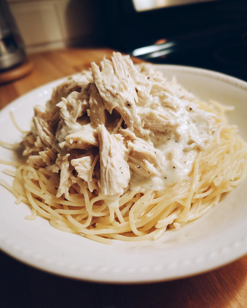 Shredded Crock Pot Angel Chicken in creamy sauce served over a bed of spaghetti noodles.