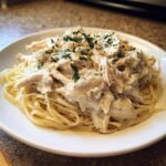 A white plate piled high with pasta topped with creamy shredded chicken from the crock pot angel chicken recipe.