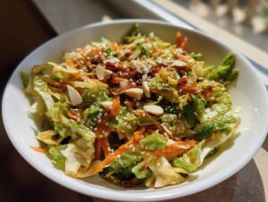 Close-up of a vibrant cabbage salad tossed in dressing, topped with slivered almonds and sesame seeds.