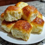 A stack of freshly baked, golden-brown dinner rolls with a shiny glaze on a white plate.