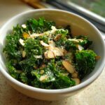 A close-up view of a vibrant green kale salad topped with slivered almonds and grated cheese.
