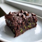 A close-up of a fudgy zucchini brownies square topped with melted chocolate chips on a white plate.