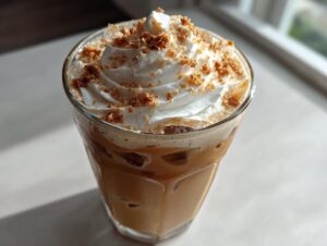 Close-up of an iced cookie butter latte topped with whipped cream and cookie crumbles.