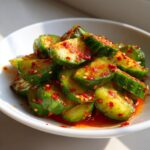Close-up of vibrant korean cucumber salad slices coated in red chili flakes and sesame seeds.