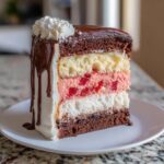 A tall slice of neapolitan cake showing layers of chocolate, vanilla, strawberry with cherries, and white cake, covered in white frosting and chocolate ganache.