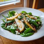 A vibrant pear salad featuring spinach, sliced pears, blue cheese crumbles, and pecans drizzled with dressing.