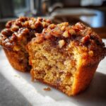 A close-up shot of a pecan pie muffin cut in half, showing the moist interior and sticky pecan topping.