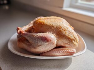 A raw, whole turkey sitting on a white plate, ready for turkey brine preparation.
