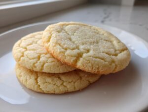 Three soft sugar cookies, slightly cracked and coated in sparkling sugar, stacked on a white plate.