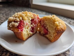 A strawberry muffin cut in half showing moist interior, fresh strawberries, and a crumb topping, perfect for strawberry muffins.