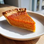 A close-up of a perfectly baked slice of sweet potato pie with a rich orange filling and crimped crust.
