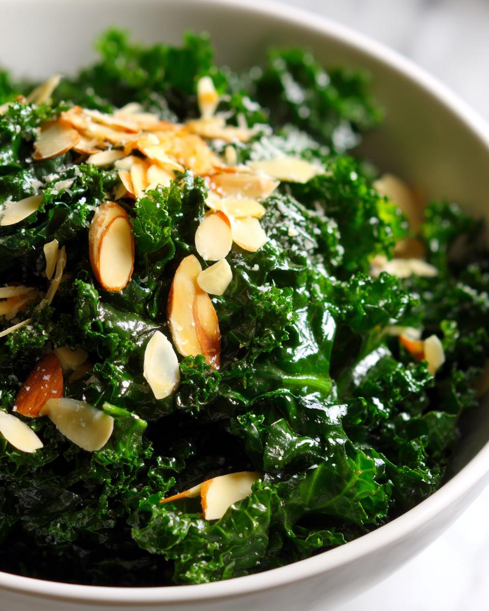 Close-up of a vibrant green kale salad topped with toasted sliced almonds in a white bowl.