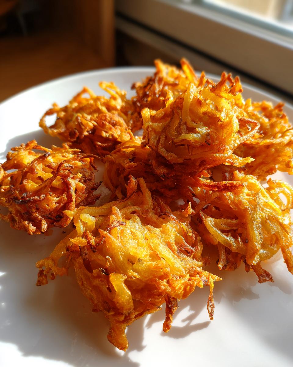 Close-up of several golden brown, crispy air fryer onion pakora piled on a white plate.
