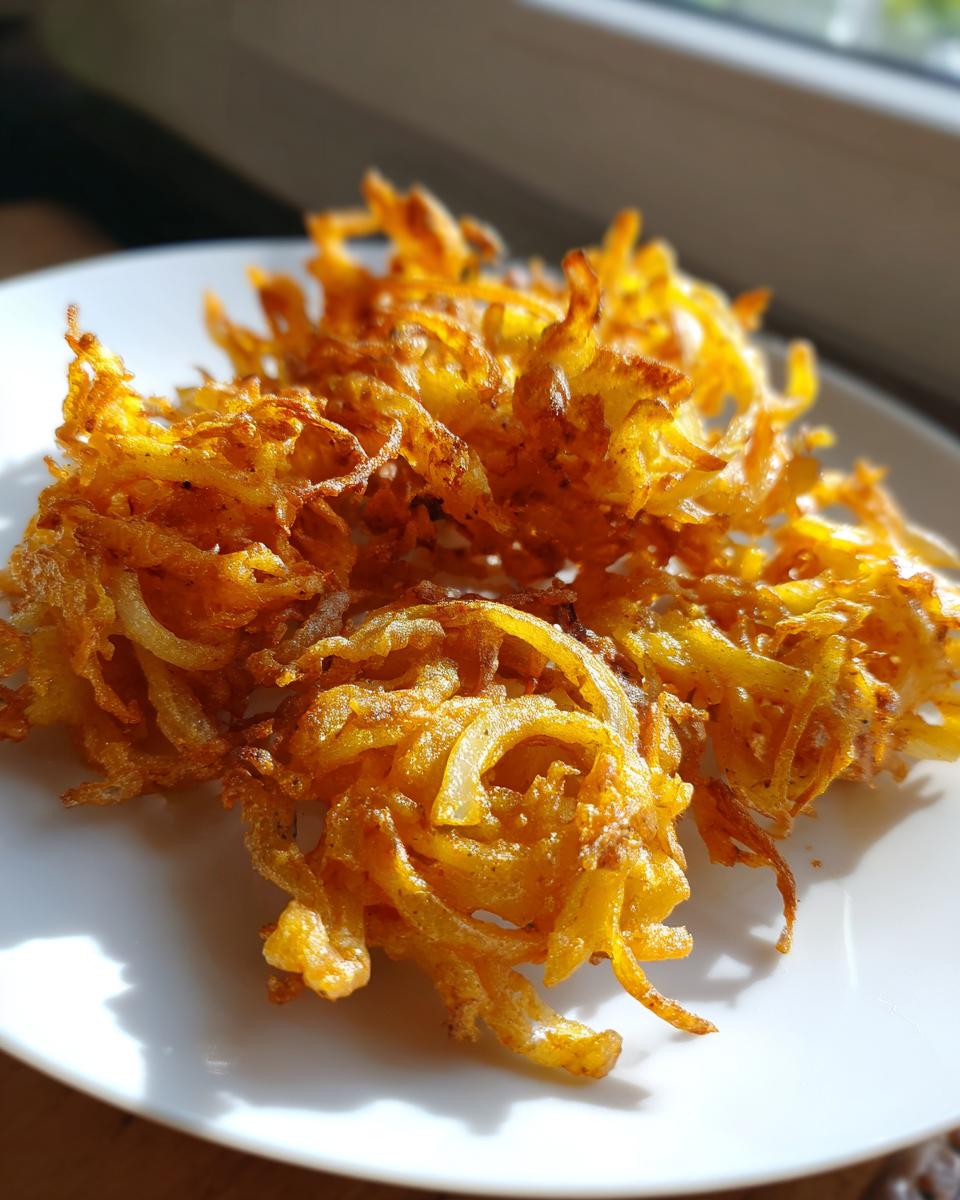 Close-up of golden brown, crispy air fryer onion pakora served on a white plate near a window.