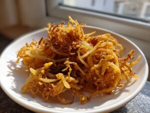 Golden brown, crispy strands of air fryer onion pakora piled on a white plate, illuminated by natural light.