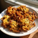 A plate piled high with crispy, golden-brown air fryer onion pakora, highlighted by bright sunlight.