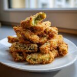 A tall stack of golden brown, crispy air fryer pickle fries piled high on a white plate.