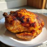 A golden brown, crispy-skinned air fryer whole roast chicken resting on a white plate.