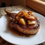 A thick, bone-in pork chop topped with caramelized apple chunks and savory sauce, representing amazing apple pork chops.