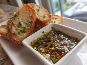 Close-up of toasted baguette slices next to a small white bowl of flavorful garlic bread dip.