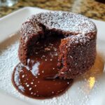 Close-up of a perfect lava cake with molten chocolate flowing out, dusted with powdered sugar.