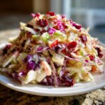 A vibrant mound of apple cranberry coleslaw featuring shredded cabbage, diced apples, and dried cranberries coated in a creamy dressing.