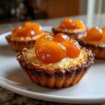 Close-up of a freshly baked apricot-almond tartlet topped with glistening apricot halves on a white plate.
