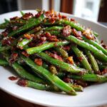 Close-up of vibrant green beans tossed in a savory, dark glaze and topped with crispy bacon bits.
