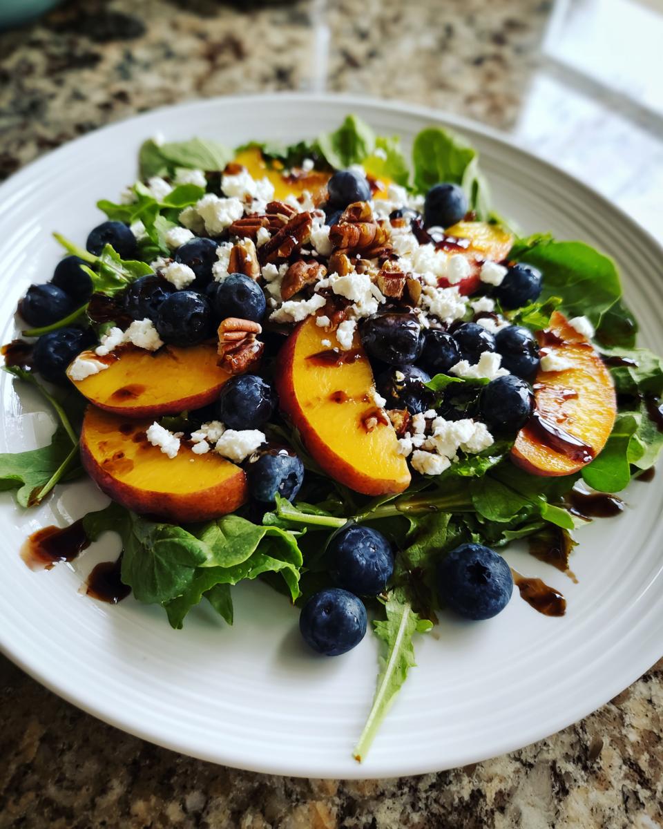 A vibrant blueberry peach feta salad served on a white plate, featuring arugula, sliced peaches, blueberries, feta, and pecans.