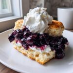 A close-up of a split biscuit topped with whipped cream, rich blueberry topping, making perfect blueberry shortcakes.