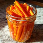Close-up of bright orange, stick-cut pickled carrots packed tightly into a clear glass mason jar.