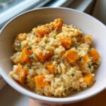 A close-up of creamy butternut squash risotto topped with orange squash cubes and fresh herbs.
