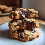 Three chewy chocolate chip almond cookies stacked, showing gooey melted chocolate filling and visible almond pieces.