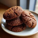 A stack of four dark, chewy gingersnap cookies coated in sugar, resting on a small plate.