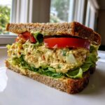 Close-up of a thick chickpea salad sandwich layered with lettuce and tomato on whole wheat bread.