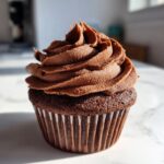 A single, perfectly baked chocolate cupcake topped with a swirl of rich chocolate frosting.