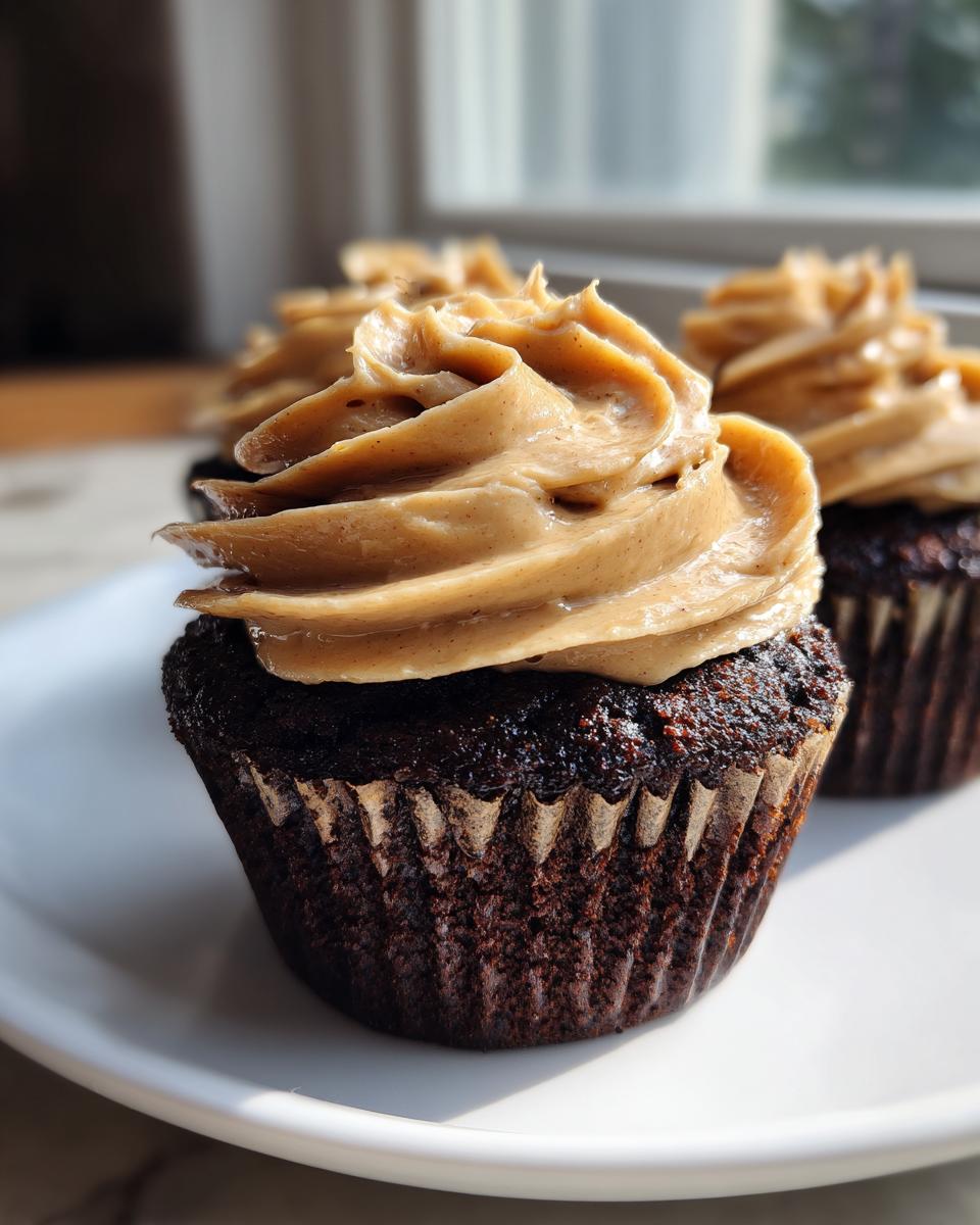 A close-up of a rich chocolate cupcake topped with swirled peanut butter frosting, part of a batch of chocolate peanut butter cupcakes.